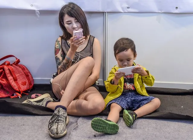 An exhibitor (L) and her son use their mobile phones as they sit in front of their stall at the China TATTOO convention in Nanning, Guangxi Zhuang Autonomous Region, China, October 24, 2015. The annual convention was held in Nanning from October 23 to 25 this year. (Photo by Reuters/Stringer)
