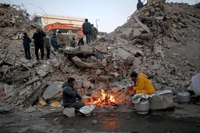 Relatives warm up around a fire in front of rubble of collapsed buildings as rescue teams continue to search victims and survivors, after a 7.8 magnitude earthquake struck the border region of Turkey and Syria earlier in the week, in Kahramanmaras on February 12, 2023. (Photo by Ozan Kose/AFP Photo)