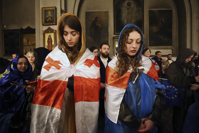 Two young women, participants in a protest against “the Russian law” and draped Georgian national flags, attend a religious service celebrating Orthodox Easter at the Trinity cathedral in Tbilisi, Georgia, late Saturday, May 4, 2024. (Photo by Zurab Tsertsvadze/AP Photo)