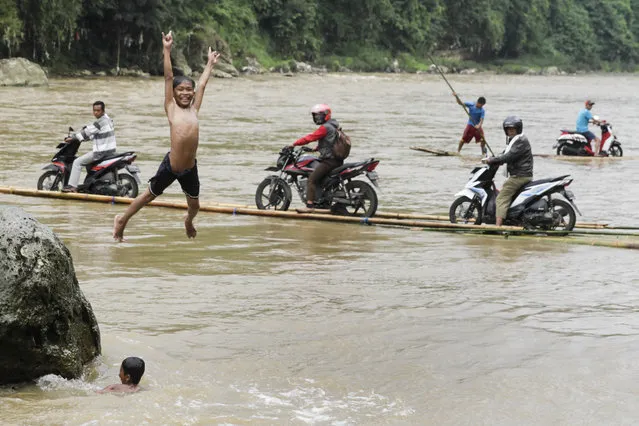 A boy jumps to the river as several people assist motorcyclists to pull up their vehicles onto wooden raft to cross Cisadane River, in Rumpin, Bogor, West Java, Indonesia on March 13, 2018. The bridge linking Rumpin – Ciseeng main roads was damaged, so the residents have to cross the river using wooden raft by paying 10,000 Rupiah (USD 0.73). (Photo by Eko Siswono Toyudho/Anadolu Agency/Getty Images)