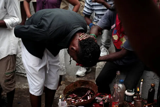 A voodoo believer is purified by cleaning his head with wine at an altar during celebrations at the cemetery of Port-au-Prince, Haiti, November 1, 2016. (Photo by Andres Martinez Casares/Reuters)