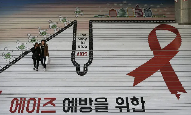 A couple passes by the red ribbon, the international symbol for AIDS awareness, on the stairs during a campaign to mark World AIDS Day in Seoul, South Korea, Tuesday, December 1, 2015. World AIDS Day is observed on Dec. 1 every year to increase awareness about the AIDS. The letters read " A campaign for the prevention of AIDS". (Photo by Ahn Young-joon/AP Photo)