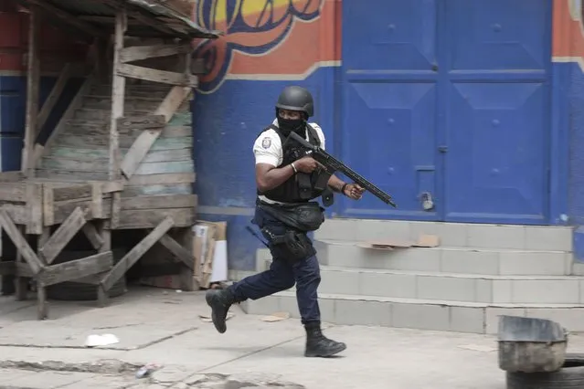 A police officer takes cover during an anti-gang operation in the Portail neighborhood of Port-au-Prince, Haiti, Tuesday, April 25, 2023, a day after a mob in the Haitian capital pulled 13 suspected gang members from police custody at a traffic stop and beat and burned them to death with gasoline-soaked tires. (Photo by Joseph Odelyn/AP Photo)