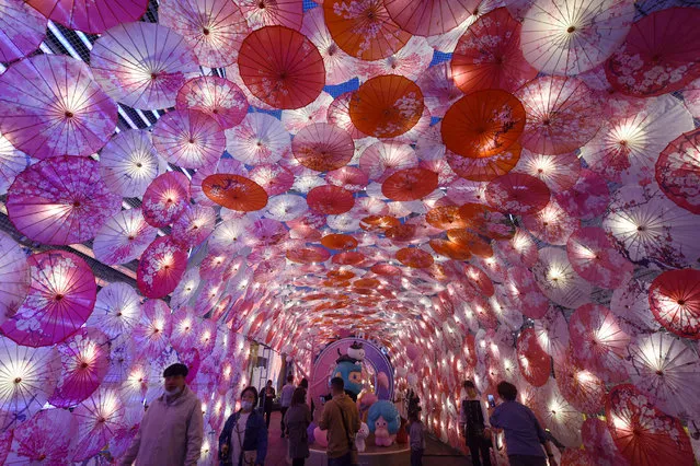 This photo taken on February 22, 2021 shows people walking past a display of umbrellas decorated with lights for the upcoming Lantern Festival on a commercial street in Hangzhou, in eastern China's Zhejiang province. (Photo by AFP Photo/China Stringer Network)