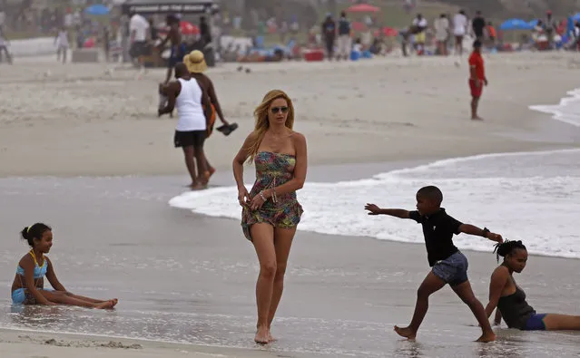 A woman walks past children playing on the beach at Camps Bay, near the city of Cape Town, South Africa, Saturday, January  24, 2015. Camps Bay  is a affluent suburb forming a integral part of the Western Cape tourist root in South Africa. (Photo by Schalk van Zuydam/AP Photo)