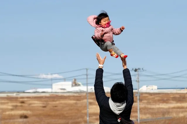 Ryo Kimura, who lost his family members, tosses his daughter, Reni Kimura, in front of a devastated area that was hit by the 2011 tsunami, during its 10th anniversary, in Namie, Fukushima prefecture, Japan on March 11, 2021. (Photo by Kim Kyung-Hoon/Reuters)