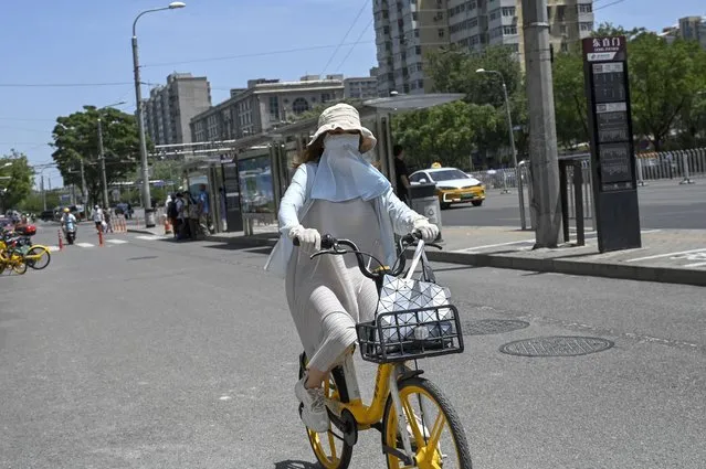 A woman wearing sun protective clothing rides a bike along a street during hot weather conditions in Beijing on July 6, 2023. (Photo by Jade Gao/AFP Photo)