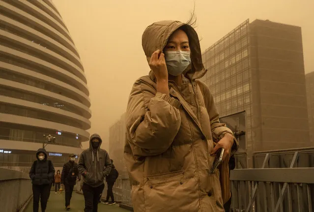 A woman wears a protective mask as she shields herself in heavy winds while commuting during a sandstorm on March 15, 2021 in Beijing, China. China's capital and the northern part of the country was hit with a sandstorm Monday, sending air quality indexes of PM 2.5 and PM 10 ratings into the thousands and cancelling flights. (Photo by Kevin Frayer/Getty Images)