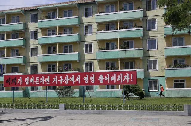 In this June 21, 2018 photo, a woman walks outside an apartment building where an anti-U.S. propaganda banner is put up in Pyongyang, North Korea. In another sign of detente following the summit between leader Kim Jong Un and U.S. President Donald Trump, North Korea has cancelled one of the most symbolic and politically charged events of its propaganda calendar: the annual “anti-U.S. imperialism” rally marking the start of the Korean War. Writings on the banner read: “If the U.S. imperialists try to invade our country, let's sweep them off the face of the Earth”. (Photo by Dita Alangkara/AP Photo)