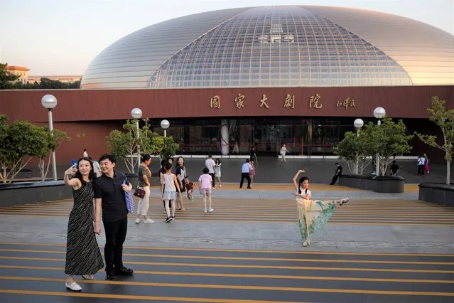 People pose for a selfie in front of the National Centre for the Performing Arts, before a performance by Russia's Bolshoi Ballet company in Beijing, China on July 25, 2023. (Photo by Thomas Peter/Reuters)