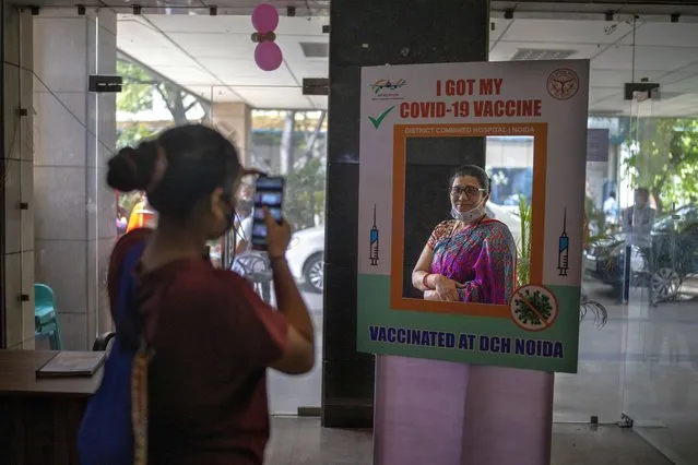 A woman poses for a photograph behind a cutout after receiving a COVID- 19 vaccine at a government hospital in Noida, a suburb of New Delhi, India, Wednesday, April 7, 2021. India hits another new peak with 115,736 coronavirus cases reported in the past 24 hours with New Delhi, Mumbai and dozens of other cities imposing night curfews to check the soaring infections. (Photo by Altaf Qadri/AP Photo)
