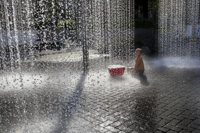 A boy cools off in a public fountain in Vilnius, Lithuania, Friday, August 18, 2023. The heat wave continues in Lithuania as temperatures rise to as high as 32 degrees Celsius (89.6 degrees Fahrenheit). (Photo by Mindaugas Kulbis/AP Photo)