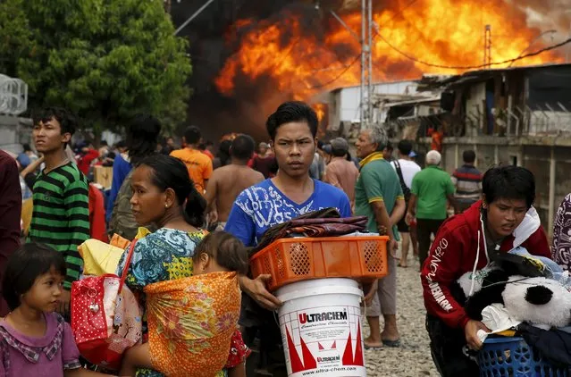 People carry their belongings away from a fire in a slum area next to railway tracks in Kampung Bandan, North Jakarta, Indonesia January 26, 2016. (Photo by Reuters/Beawiharta)