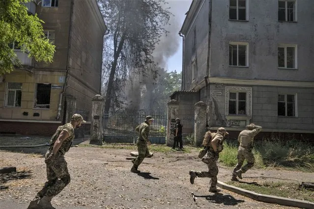 Ukrainian soldiers run after a missile strike hit a residential area, in Kramatorsk, Donetsk region, eastern Ukraine, Thursday, July 7, 2022. Injured residents sat dazed and covered in blood. A crater was now the centre of the courtyard. Last week, the governor of the Donetsk oblast Pavlo Kyrylenko urged the province's more than 350,000 remaining residents to flee to safer towns further West, saying that evacuating the region was necessary to save lives and allow the Ukrainian army to better defend towns against a Russian advance. Many refuse to leave the city. (Photo by Nariman El-Mofty/AP Photo)