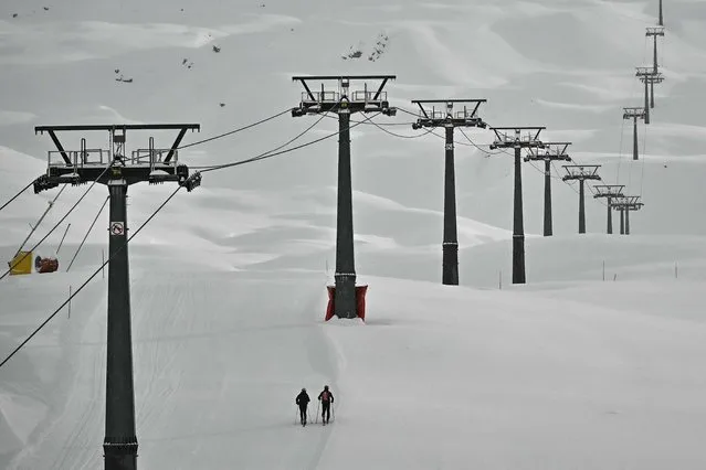 Two persons walk on a track under ski-lifts in the ski resort of Cervinia on November 11, 2023 after the men's downhill was cancelled due to heavy snow last night during the FIS Alpine Ski World Cup in close  Zermatt-Cervinia. (Photo by Marco Bertorello/AFP Photo)