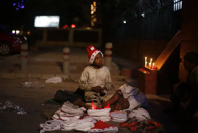 A young Indian boy sells Christmas merchandise outside the Sacred Heart's Cathedral in New Delhi, India, Tuesday, December 24, 2013. Though Hindus and Muslims comprise the majority of the population in India, Christmas is celebrated with much fanfare. (Photo by Altaf Qadri/AP Photo)