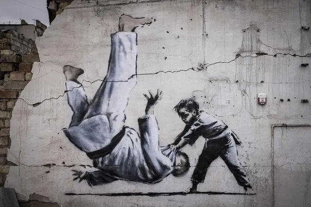 Graffiti of a child throwing a man on the floor in judo clothing is seen on a wall amid damaged buildings in Borodyanka on November 11, 2022 in Kyiv Region, Ukraine. The art work has sparked online speculation over whether the graffiti artist Banksy has been working in Ukraine. Borodyanka was hit particularly hard by Russian airstrikes in the first few weeks of the conflict. Electricity and heating outages across Ukraine caused by missile and drone strikes to energy infrastructure have added urgency to preparations for winter. (Photo by Ed Ram/Getty Images)