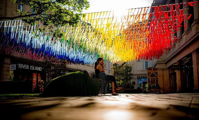 A person sits beneath rainbow coloured street decorations as the strong morning sun casts shadows on the floor in Bath city centre, United Kingdom on Wednesday, September 8, 2021. (Photo by Ben Birchall/PA Images via Getty Images)