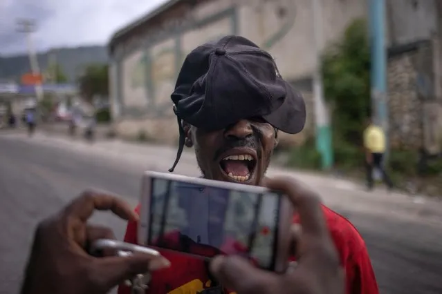 A man, part of group of locals who set up a barricade to protest against fuel shortages, covers his face as he speaks to a man recording video on a mobile device in Port-au-Prince, Haiti on October 21, 2021. (Photo by Adrees Latif/Reuters)