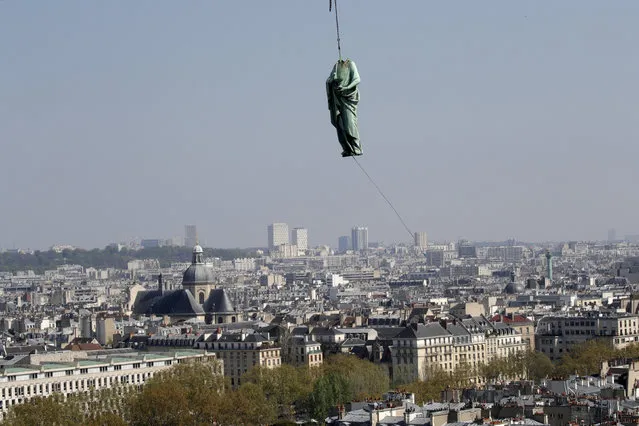 The religious statue representing St. Andrew perched atop Paris' Notre Dame Cathedral descends to earth for the first time in over a century as part of a restoration, in Paris Thursday, April 11, 2019. The 16 greenish-gray copper statues, which represent the twelve apostles and four evangelists, are lowered by a 100 meter (105 yard) crane onto a truck to be taken for restoration in southwestern France. (Photo by Philippe Wojazer/Reuters)