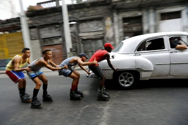 Teenagers on roller skates hold on to each other as they are pulled by a vintage car to move along a street in Havana, Cuba March 19, 2016. (Photo by Ivan Alvarado/Reuters)