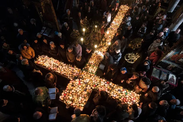 Believers pray around a cross-shaped platform covered with candles placed in jars of honey during a ceremony marking the day of Saint Haralampi, Orthodox patron saint of bee-keepers, at the Church of the Blessed Virgin in Blagoevgrad, eastern Bulgaria, on February 10, 2017. (Photo by Nikolay Doychinov/AFP Photo)
