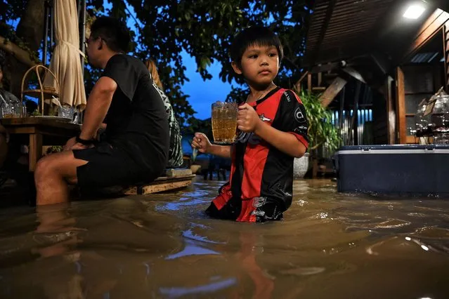 This photo taken on October 7, 2021, shows a young customer carrying a drink at the Chaopraya Antique Cafe, as flood water from the Chao Phraya River surges into the restaurant, in Nonthaburi province north of Bangkok. (Photo by Lillian Suwanrumpha/AFP Photo)