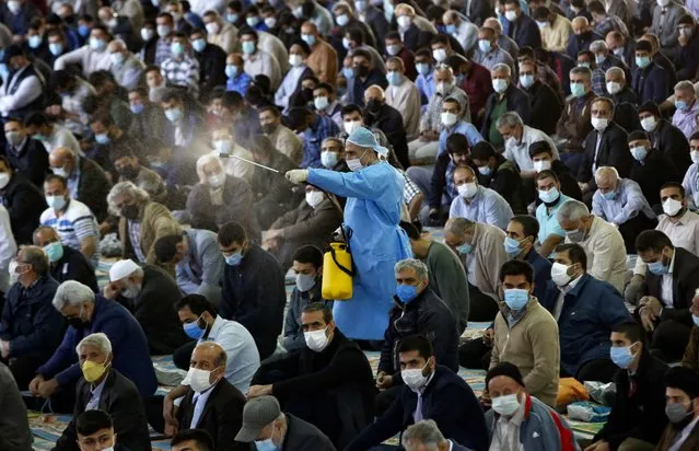 A municipal worker sprays disinfectant as mask-clad Iranians gather in a mosque in the capital Tehran to perform the Friday prayers, for the first time after authorities eased some restrictions put in place for over a year in a bid to stem the spread of the coronavirus, on October 22, 2021. (Photo by AFP Photo/Stringer)