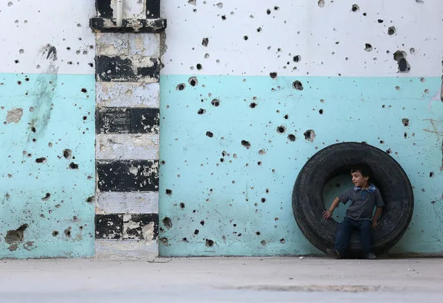 A boy sits on a wheel in front of the bullet-riddled facade of a mosque on the first day of Eid al-Adha in the Duma neighborhood in Damascus October 4, 2014. (Photo by Bassam Khabieh/Reuters)