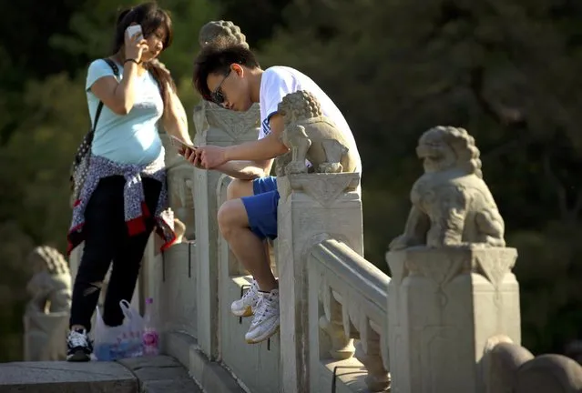 Chinese teenagers use their smartphones as they stand on a bridge decorated with carved stone lions at the Fragrant Hills Park in suburban Beijing, Monday, May 4, 2015. The park, once the home of imperial gardens for China's emperors, is now an attraction popular with both locals and tourists in Beijing. (Photo by Mark Schiefelbein/AP Photo)