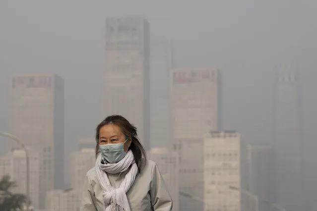 A woman wearing a face mask to protect from COVID-19 walks against the office buildings in Central Business District shrouded by pollution haze in Beijing, Thursday, November 18, 2021. (Photo by Andy Wong/AP Photo)