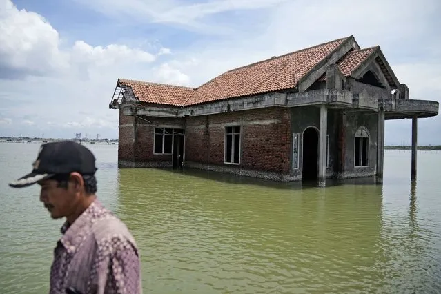 A man walks past a house abandoned after it was inundated by water due to the rising sea level in Sidogemah, Central Java, Indonesia, Monday, November 8, 2021. World leaders are gathered in Scotland at a United Nations climate summit, known as COP26, to push nations to ratchet up their efforts to curb climate change. Experts say the amount of energy unleashed by planetary warming would melt much of the planet's ice, raise global sea levels and greatly increase the likelihood and extreme weather events. (Photo by Dita Alangkara/AP Photo)