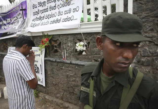 A relative of an Easter Sunday bomb blast victim prays after placing the flowers on the wall of St. Sebastian's Church in Negombo, north of Colombo, Sri Lanka, Sunday, April 28, 2019. Sri Lanka's Catholics celebrated Sunday Mass in their homes by a televised broadcast as churches across the island nation shut over fears of militant attacks, a week after the Islamic State-claimed Easter suicide bombings killed over 250 people. Banner in Sinhalese reads, “those innocents who went to church in the break of the day with thousands of expectations had to depart to the almighty”. (Photo by Manish Swarup/AP Photo)