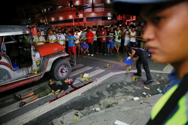 Onlookers gather as police investigate the scene around a body of a man killed by unknown gunmen in Manila, Philippines early October 18, 2016. A sign on a cardboard found near the body reads, “Pusher Ako, Wag Tularan”, which translates to “I am a (drug) pusher, don't be like me”. (Photo by Damir Sagolj/Reuters)