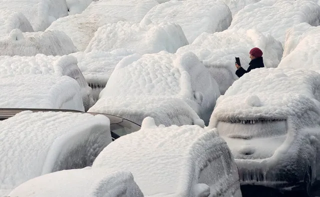 A woman takes a picture of ice-covered vehicles unloaded from the cargo ship Sun Rio, which was caught in severe weather conditions in the Sea of Japan, in the port of Vladivostok, Russia on December 29, 2021. (Photo by Tatiana Meel/Reuters)