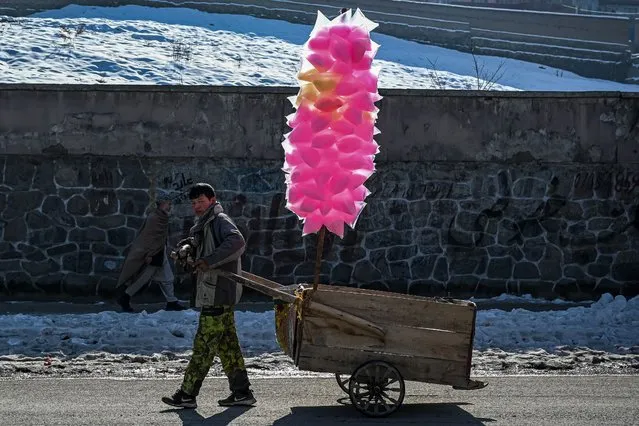 An Afghan boy pulls a cart containing cotton candy sweets along a street in Kabul on January 14, 2022. (Photo by Mohd Rasfan/AFP Photo)