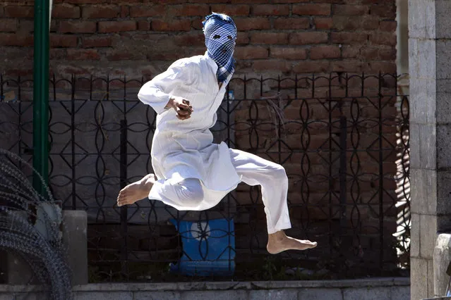 A Kashmiri masked Muslim protester jumps in the air to avoid stones thrown at him by Indian police during a protest in Srinagar, Indian controlled Kashmir, Friday, April 29, 2016. Government forces fired tear gas and pellet guns to stop rock-throwing Kashmiri youths after Friday prayers. The demonstrators were responding to a protest call by anti-India separatist leaders against, what they said, government's failure to arrest the troops involved in the recent killing of five civilians following an alleged molestation of a teenage girl student by an Indian soldier. (Photo by Dar Yasin/AP Photo)