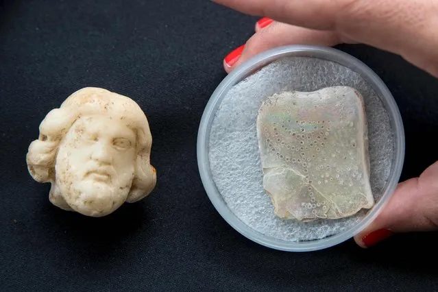 A picture taken on April 26, 2017, shows the head part of a figurine (L) from the Roman period depicting the Asclepius, god of medicine and a small tablet engraved with a seven-branched menorah, discovered during the renovation of the ancient harbour of Caesarea, being displayed during a press conference in the Israeli Mediterranean town of Caesarea. (Photo by Jack Guez/AFP Photo)