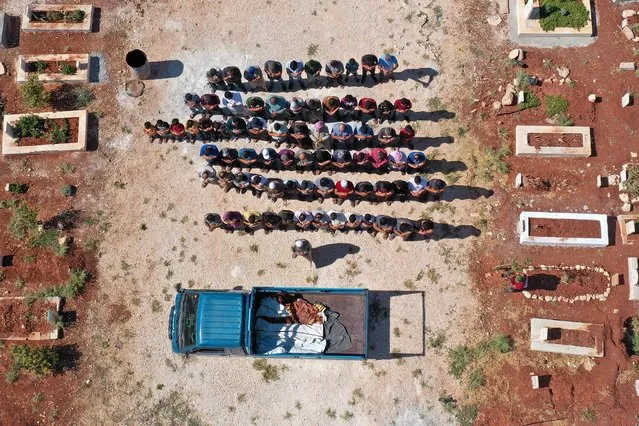 An aerial view shows mourners praying over the bodies of three children, who were killed in regime artillery shelling on the outskirts of Fuaa town, during a funeral procession at a cemetery in Binnish in Syria's rebel-held northwestern province of Idlib on July 15, 2021. Shelling by Syrian regime forces killed nine civilians, including three children, in the Idlib region of the country's northwest, a war monitor reported The deaths come amid an uptick in violations of a ceasefire deal that was brokered by Turkey and Russia in March 2020 and had since largely held. (Photo by Omar Haj Kadour/AFP Photo)