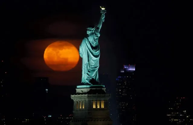 The full Worm Moon rises behind the Statue of Liberty in New York City on March 18, 2022, as seen from Jersey City, New Jersey. (Photo by Gary Hershorn/Getty Images)