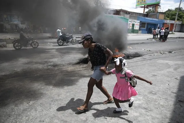 A woman guides a child past a demonstration against increasing violence in Port-au-Prince, Haiti, Tuesday, March 29, 2022. The protest coincides with the 35th anniversary of Haiti’s 1987 Constitution and follows other protests and strikes in recent weeks in the middle of a spike in gang-related kidnappings. (Photo by Odelyn Joseph/AP Photo)