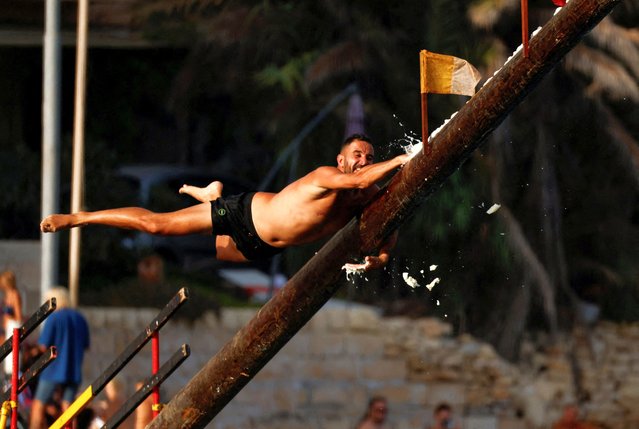 A competitor tries to grab a flag as he falls off the “gostra”, a pole covered in lard, during the celebrations of the religious feast of St. Julian, patron of the town of St. Julian's, Malta on August 18, 2024. (Photo by Darrin Zammit Lupi/Reuters)