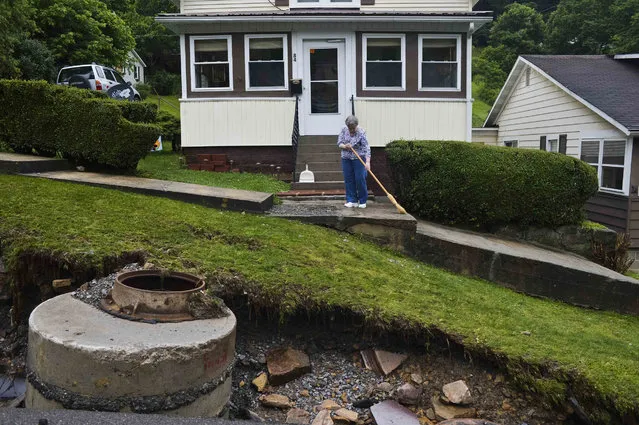 Cookie Waselchalk sweeps pebbles and small rocks from her doorstep after flood waters ripped away large portions of her front yard and asphalt in Richwood, W.Va. on Friday June 24, 2016. (Photo by Christian Tyler Randolph/Charleston Gazette-Mail via AP Photo)