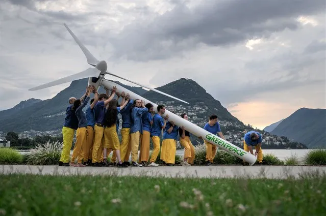 Greenpeace activists raise a factice wind turbine on the edge of Lake Lugano during a demonstration calling for a sustainable reconstruction of Ukraine, on the sideline of a two-day Ukraine Recovery Conference in Lugano on July 4, 2022. Ministers from dozens of countries and international organisations leaders will gather in the city of Lugano with the aim of providing a roadmap for the war-ravaged country's recovery. (Photo by Fabrice Coffrini/AFP Photo)