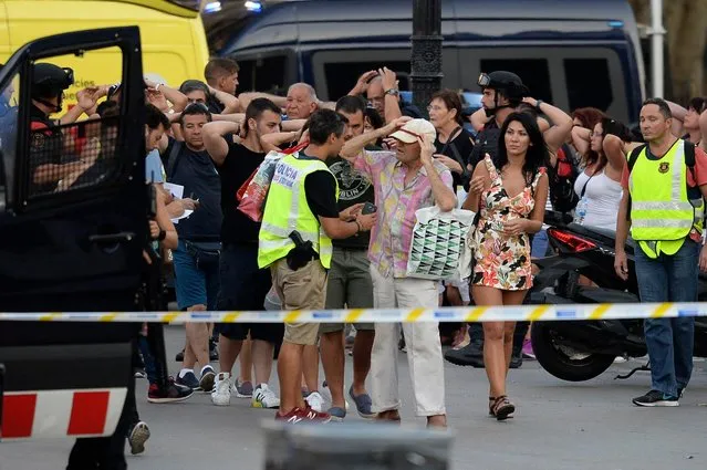 Policemen check the identity of people standing with their hands up after a van ploughed into the crowd, killing two persons and injuring several others on the Rambla in Barcelona on August 17, 2017. A driver deliberately rammed a van into a crowd on Barcelona' s most popular street on August 17, 2017 killing at least two people before fleeing to a nearby bar, police said. .Officers in Spain' s second- largest city said the ramming on Las Ramblas was a “terrorist attack” and a police source said one suspect had left the scene and was “holed up in a bar”. The police source said they were hunting for a total of two suspects. (Photo by Josep Lago/AFP Photo)