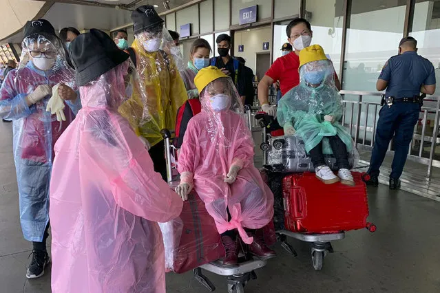 A Chinese family covered with plastic bags as a precautionary measure against the new coronavirus walk at the departure level of Manila's International Airport, Philippines on Wednesday, March 18, 2020. The Philippine government lifted a 72-hour deadline for thousands of foreign travelers to leave the country's main northern region which has been placed under quarantine due to the growing number of coronavirus infections, officials said. (Photo by Joeal Calupitan/AP Photo)