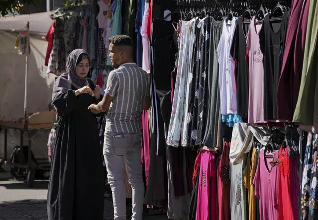 A women buys clothes on the main road of an outdoor clothes market in Gaza City, Monday, July 25, 2022. Gaza's Hamas rulers have imposed a slew of new taxes on imported clothes and school supplies just ahead of the new school year, sparking limited but rare protests in the impoverished coastal area. (Photo by Adel Hana/AP Photo)