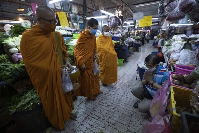 A Thai Buddhist prays after offering food to Thai Buddhist monks as they wear face masks to protect themselves from a new coronavirus in Bangkok, Thailand, Wednesday, March 25, 2020. Thailand's government agreed to declare an emergency to take stricter measures to control the coronavirus outbreak that has infected hundreds of people in the Southeast Asian country. (Photo by Sakchai Lalit/AP Photo)