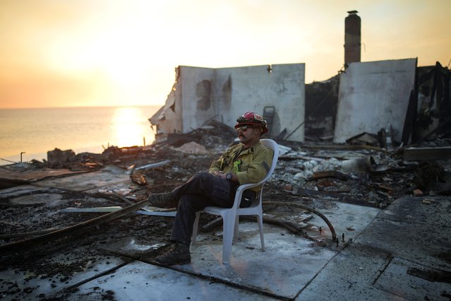 A firefighter sits on a chair amid the remains of a burnt structure along the Pacific Coast Highway in Malibu, on January 8, 2025. (Photo by Daniel Cole/Reuters)