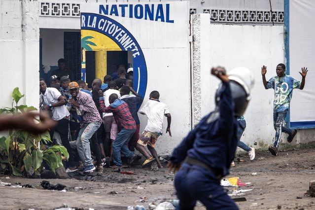 A Police officer throws a rock as opposition supporters run into a opposition leader Martin Fayulu’s party house during a demonstration in Kinshasa on December 27, 2023. Police were deployed in the Democratic Republic of Congo's capital Kinshasa on December 27, 2023 during a banned demonstration against recent elections in the fragile central African state.Leading opposition politicians in impoverished but mineral-rich DRC have rejected last week's vote, which was marred by severe delays and bureaucratic disarray, and called for a demonstrations. (Photo by John Wessels/AFP Photo)